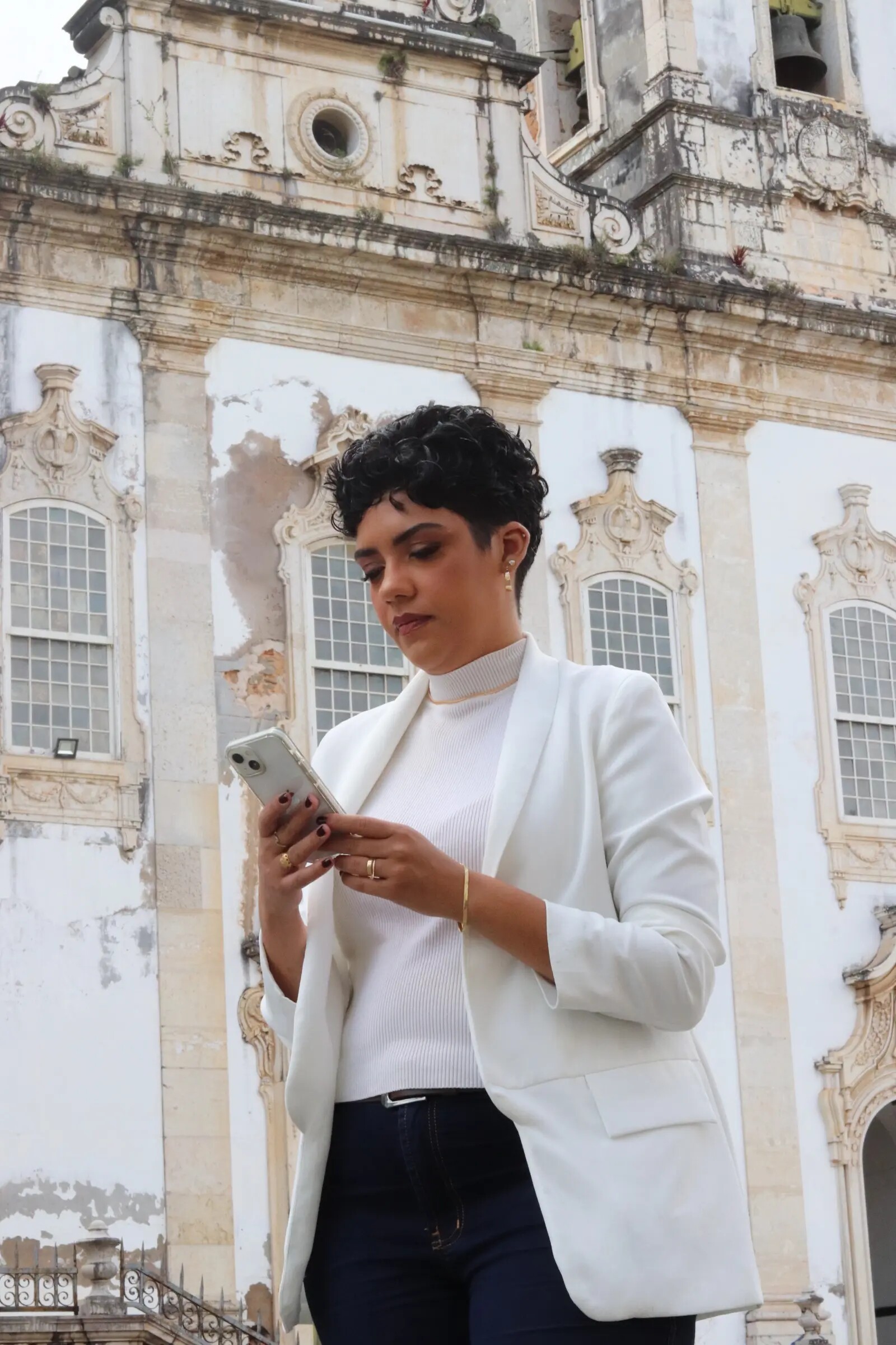 Julyane Andrade diante de edificação histórica, com cabelo curto e cacheado